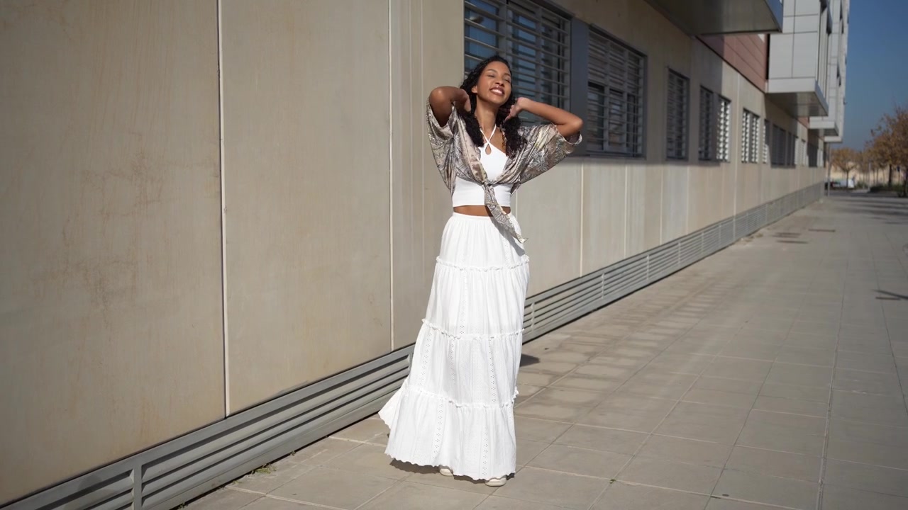 Una donna elegante con un abito bianco svolazzante che posa all'aperto sotto una luce naturale intensa.