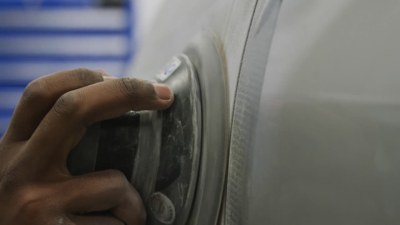 African American male car mechanic wearing a face mask and polishing a side of a car with a grinder