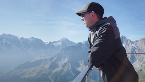 the depiction showcases a youthful man relishing the captivating sight of a cliff nestled amidst majestic mountains, magnificently adorned with a shimmering blanket of snow