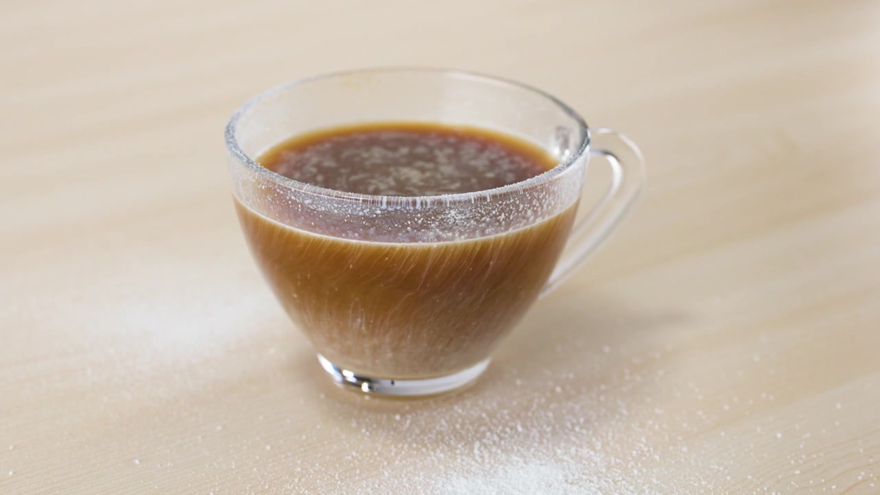 Primo piano di panna vegetale bianca che si mescola nel caffè nero caldo in una tazza di vetro