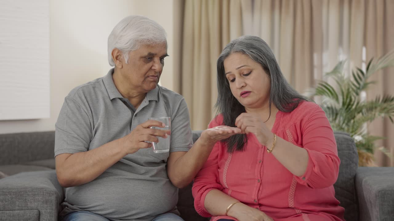 un marido indio le da medicina a su vieja esposa enferma.