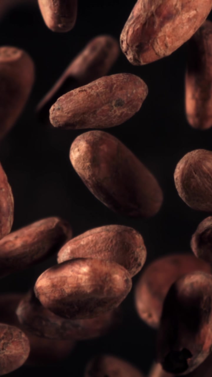 Primer plano a cámara lenta de granos de cacao cayendo sobre un fondo oscuro.