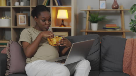 pregnant woman snacking and watching laptop