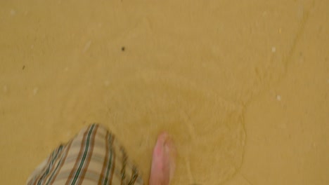 caucasian man's foot walking on the beach while waves flush his feet, high eagle, real time