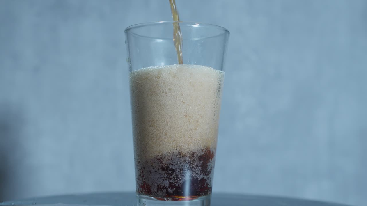 soda de raiz de cerveja derramada em um copo alto, com o líquido de âmbar criando um topo cremoso e espumoso