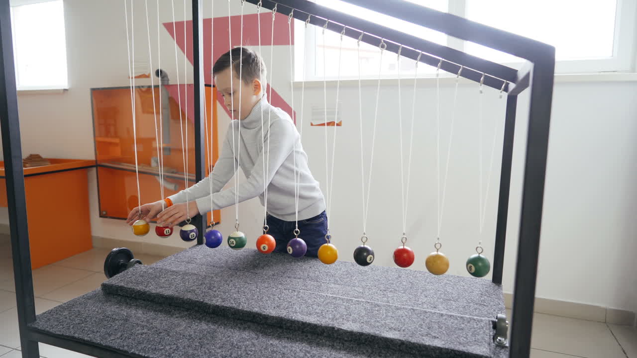 Boy makes an experiment with Newton's pendulum. The concept of physics. Museum of Science