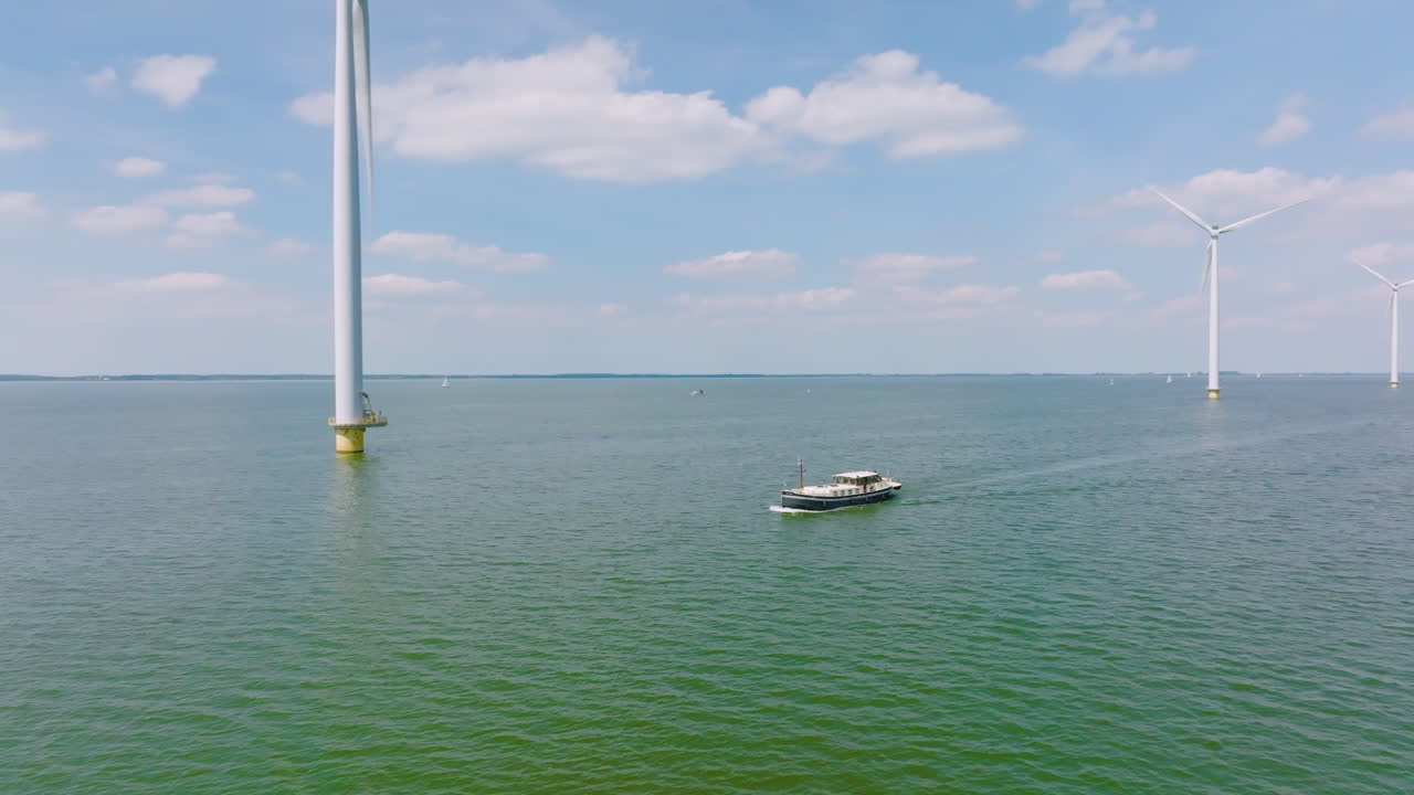 A traveling ship sails under wind turbines in calm water