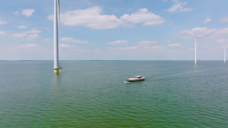 A traveling ship sails under wind turbines in calm water