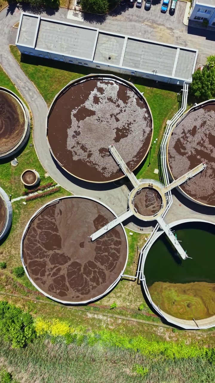 Planta de tratamiento de aguas que muestra grandes tanques circulares utilizados para procesar aguas residuales y una zona verde cercana en un día soleado