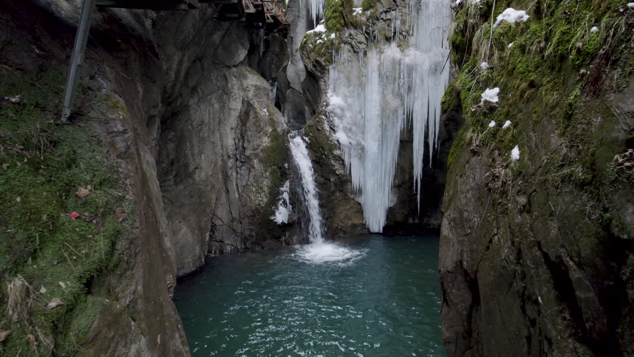 drone volando hacia una pequeña cascada y un lago de agua azul entre acantilados con musgo y hielos en austria en el sigmund thun klamm