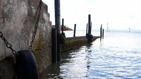 neumáticos encadenados en la pasarela del embarcadero del puerto de madera desgastada con la marea tranquila dolly lento a la izquierda