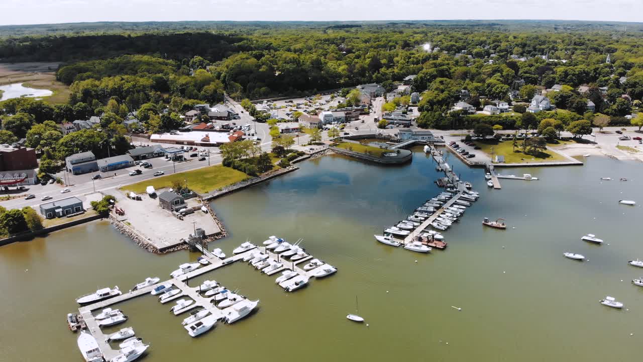 Seaside community as viewed by drone on a sunny summer day, with the green harbor below with watercraft and activity