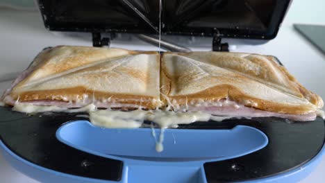 cerrar con manos de hombre abriendo sandwichera preparando dos sándwiches