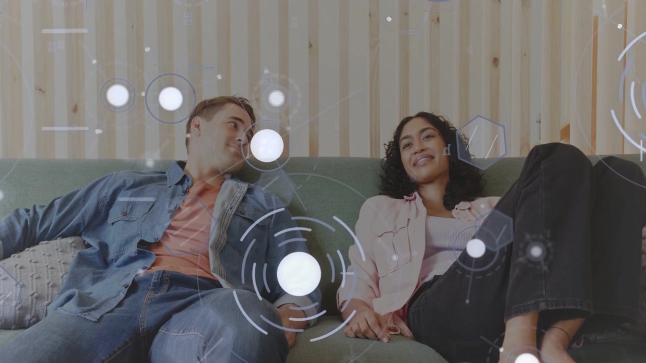 Man and woman reclining on green sofa, woman reaching circular HUD and demoing tech interface