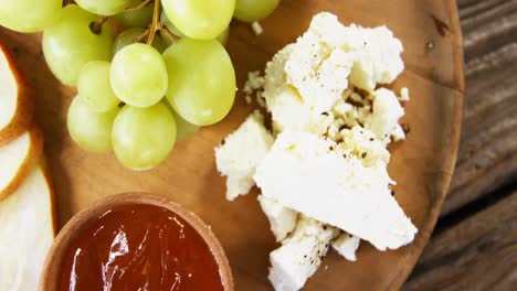 cheese with grapes, apple slices, walnuts and sauce on wooden plate