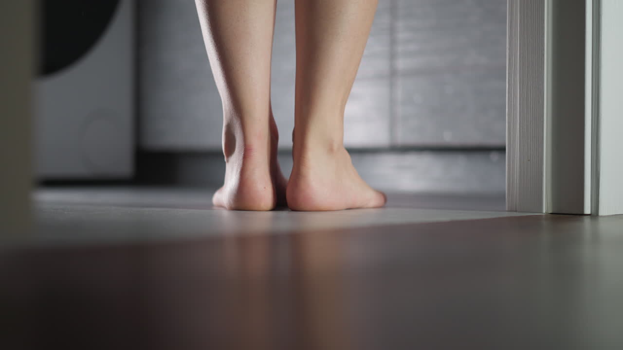 Barefoot woman stands in bathroom doorway closeup. Elegant lady prepares to take bath at home. Flirty woman stands puts on tiptoe entering room