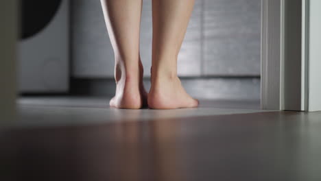 barefoot woman stands in bathroom doorway closeup. elegant lady prepares to take bath at home. flirty woman stands puts on tiptoe entering room