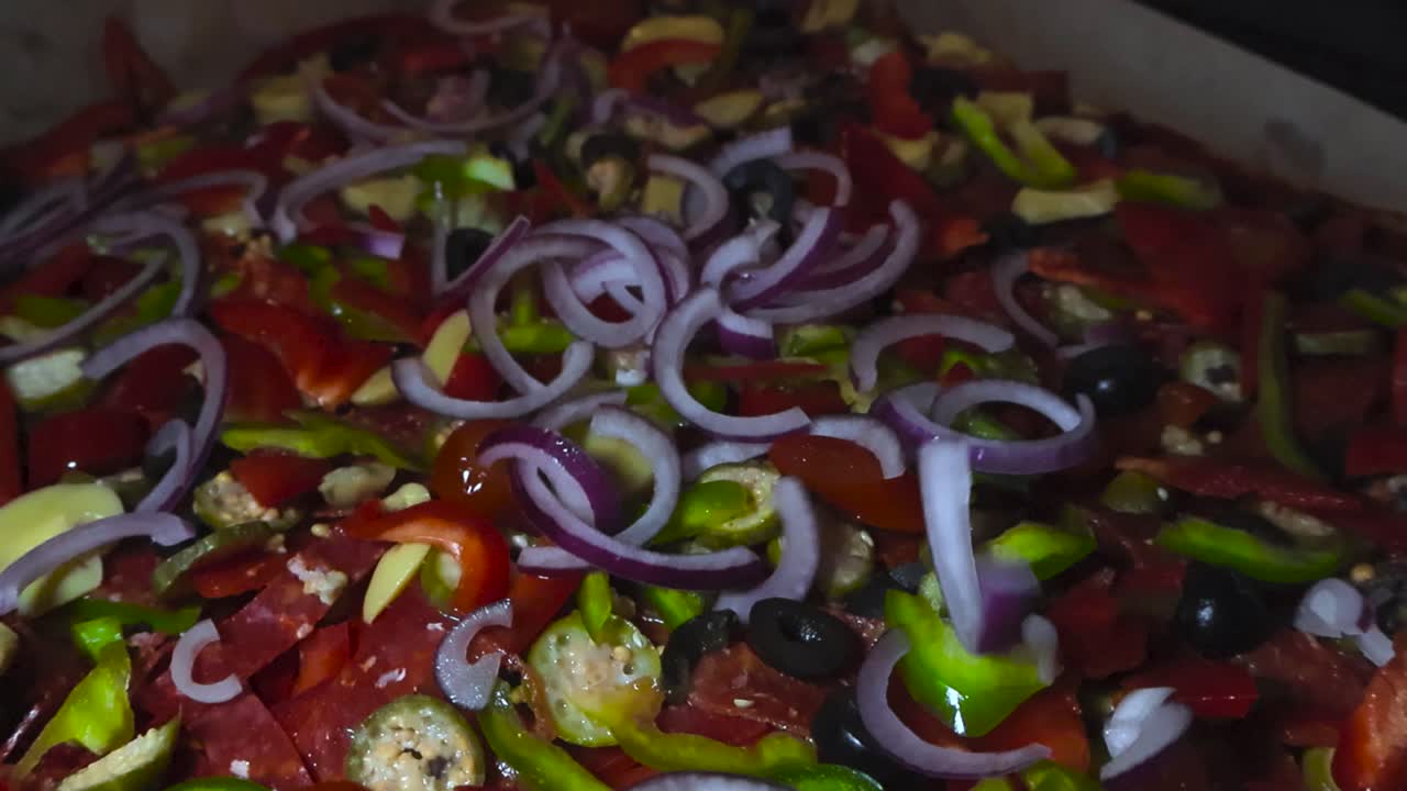 Close up view of red onion sliced being dropped on other pizza topping on freshly cooked and baked dough with shallow depth of field and bokeh background. Paprikas, jalapenos and mushrooms visible