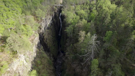 aerial drone shot flying away from waterfall inside narrow corrieshalloch gorge surrounded by forest in scottish highlands