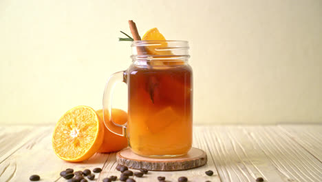 un vaso de café negro americano helado y una capa de jugo de naranja y limón decorado con romero y canela