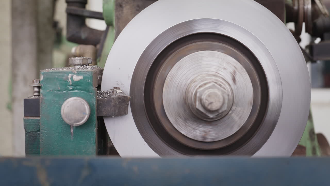Primo piano di un tornio industriale che taglia un disco di metallo con trucioli volanti.
