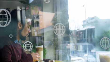 animación de iconos del globo sobre hombre biracial bebiendo café mientras mira a través de una ventana de vidrio