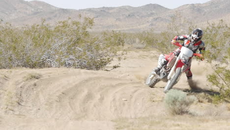 slow motion: a dirt biker rides his crf honda through the desert and whips around a berm