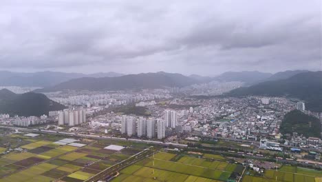 busan city skyline with surrounding mountains and fields under a cloudy sky, aerial view