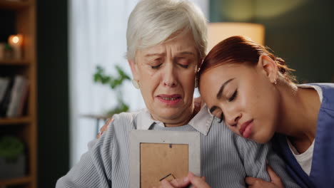 a caregiver comforts a senior woman grieving over a photo