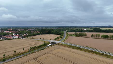 white truck on rural road of american town. suburb district with harvested wheat fields in summer. aerial wide shot. small historic town in background. iowa, usa