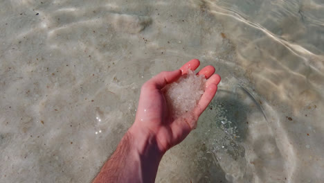 male hand grabs thick silica salty sand from the dead sea raises to view