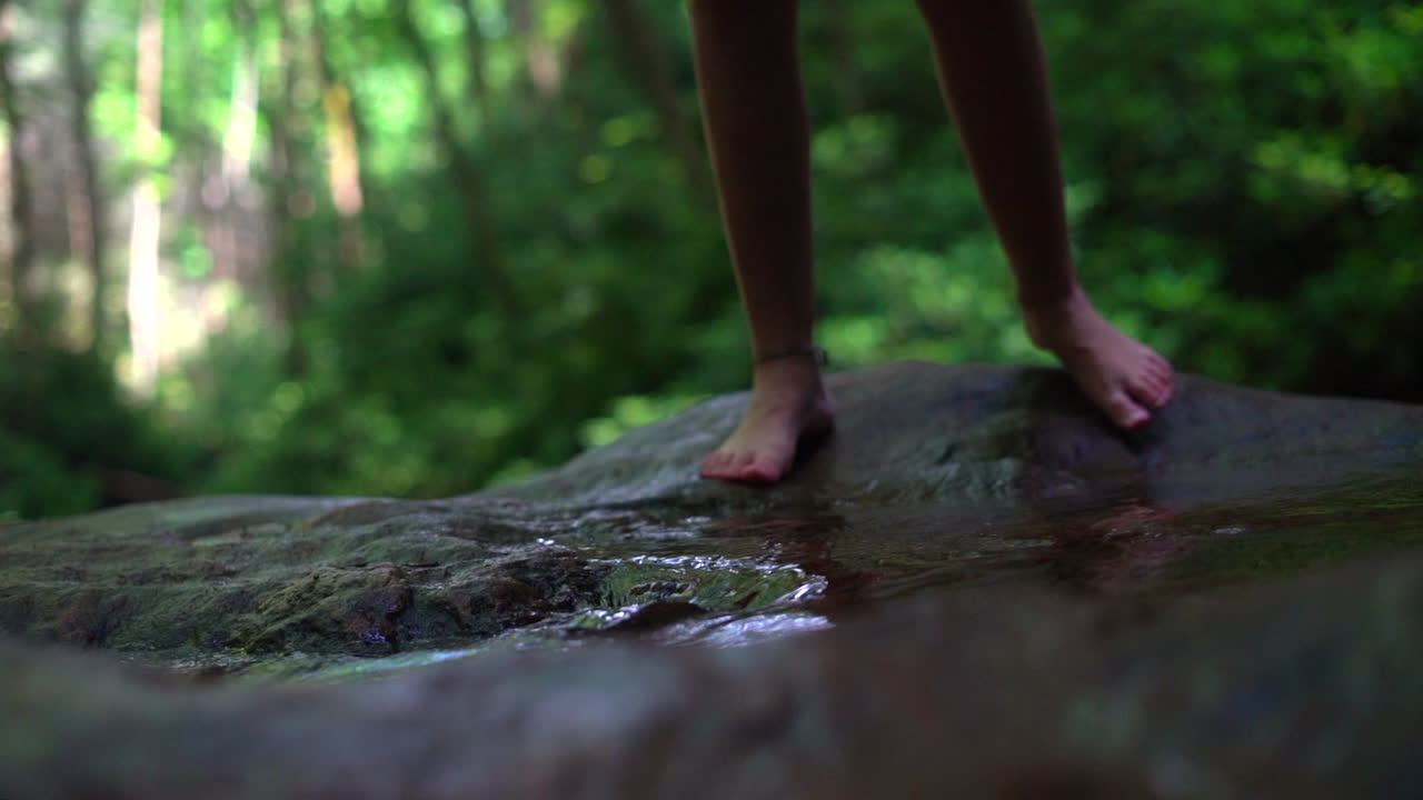 Woman's feet seen stepping into a shallow stream in the forest - slow motion