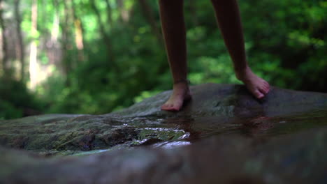 woman's feet seen stepping into a shallow stream in the forest - slow motion