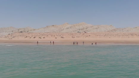 aerial over waters with people wading from golden beach in balochistan