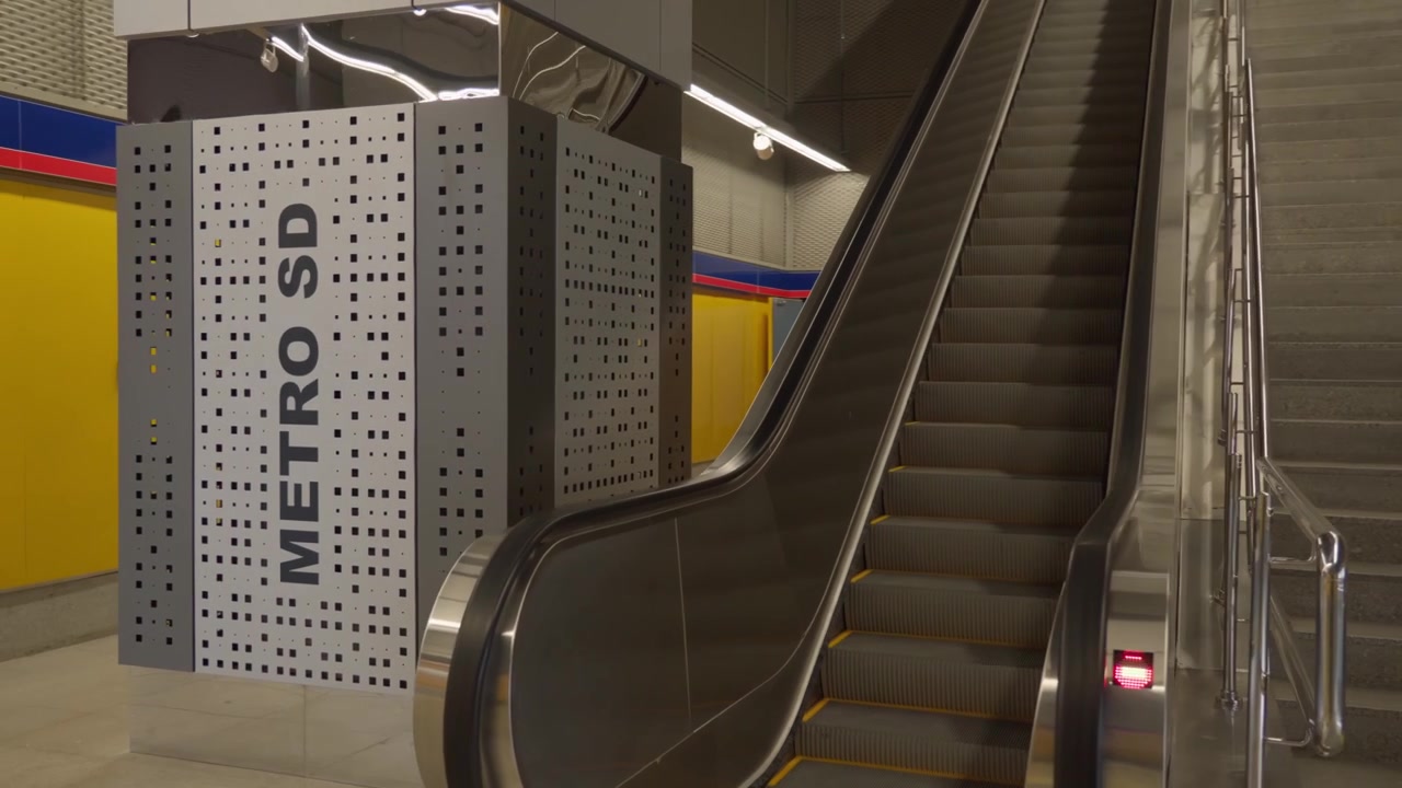 Una carrellata dell'interno di una moderna stazione della metropolitana che mostra scale mobili, scale in cemento e la segnaletica della stazione.