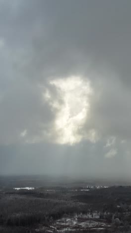 sun rays breaking through thick clouds in winter. vertical aerial view over the countryside landscape. snow storm approaching. dramatic sky over the forest.