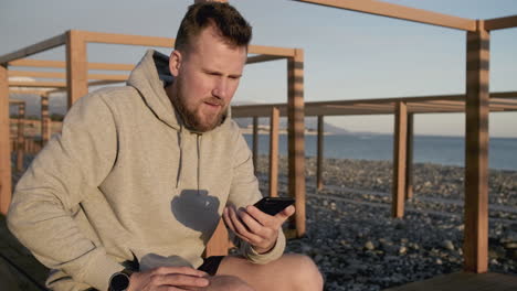 man using phone on the beach at sunset