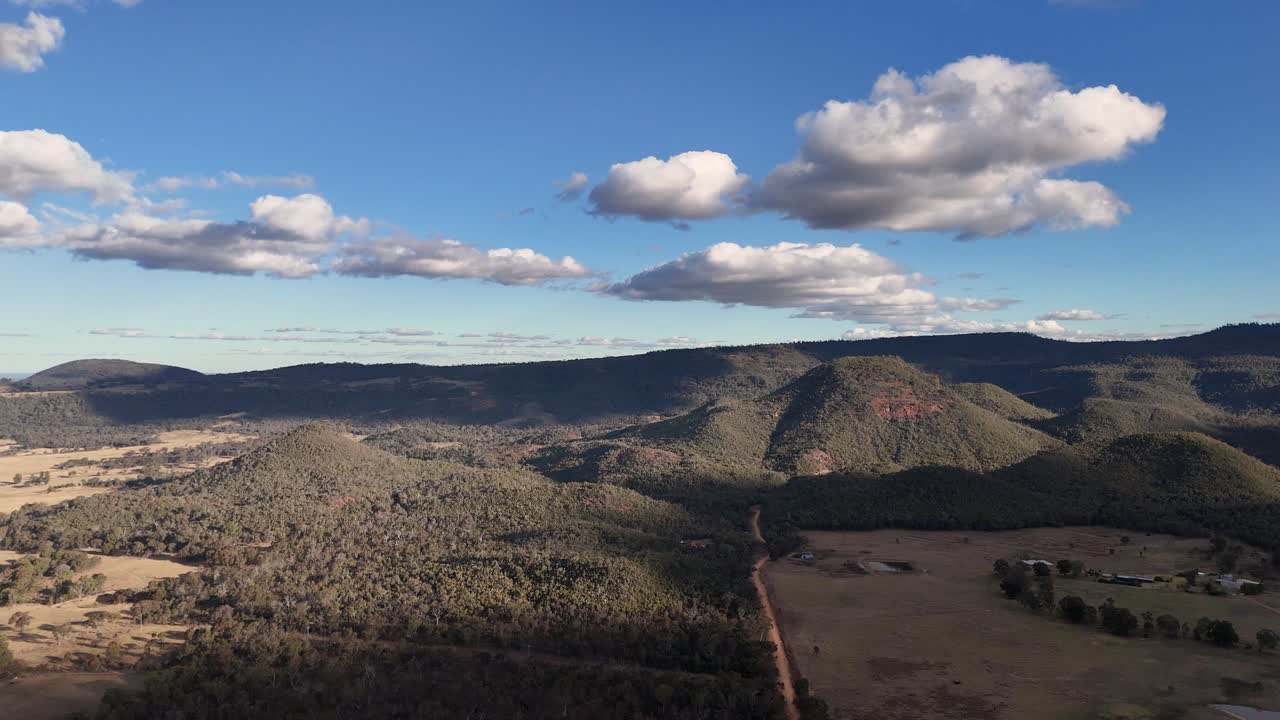 Drone footage glides above rugged mountain terrain and forested hills in New South Wales, Australia, under bright daylight with scattered clouds and clear visibility