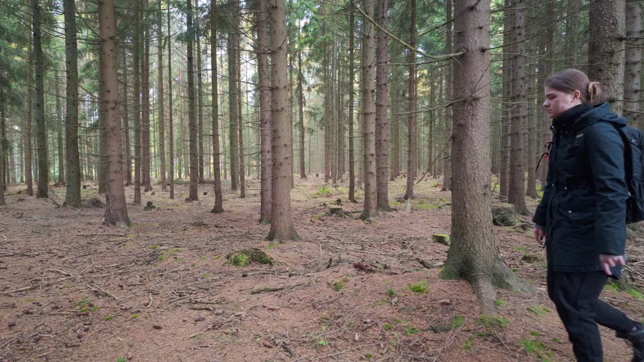 En kvinne med en ryggsekk går gjennom en mørk skog på en fottur. En tur i naturen om høsten