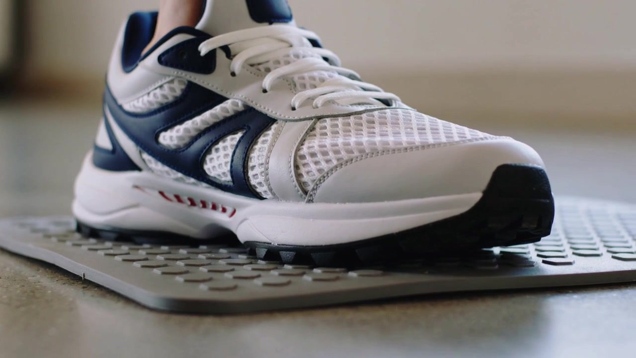 Abbassare una sneaker bianca e blu scuro, premendo l'avampiede su un tappetino testurizzato nella stanza, caricando il peso per fare un passo.
