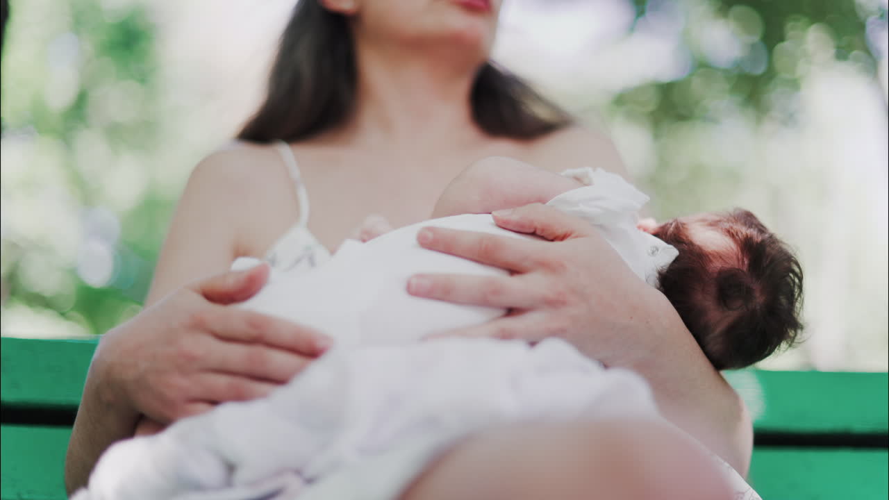 Tender moment of a mother breastfeeding her baby on a green park bench in daylight