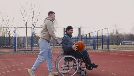 young disabled man bouncing the ball and throwing it into the basketball hoop while his friend pushing him