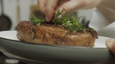 chef decorates steak dish with rosemary leaves