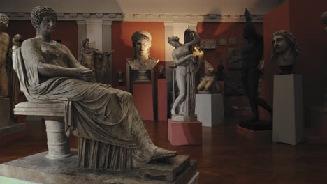 ancient antique statues of an old and a young woman in a museum with moody warm lights and more statues and figurines in the background