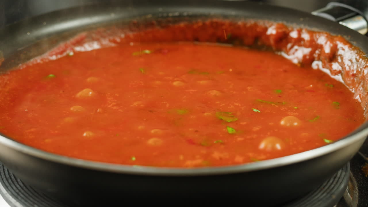 Chicken in tomato sauce is boiling on a frying pan with spices. Cooking tomato sauce curry with chicken fillet. Traditional Italian Mexican Asian dish. High quality studio shot for cafe, restaurant close up.