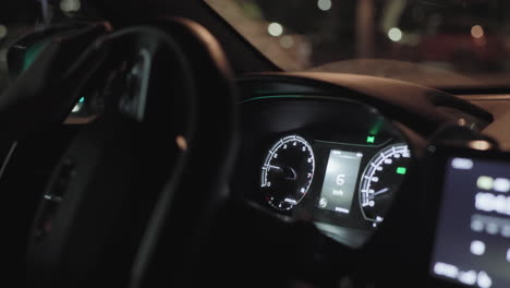 close up of driver turning steering wheel inside moving car at night with illuminated dashboard, digital speedometer, and blurred street lights visible through windshield