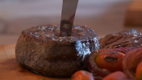 Close-up-of-a-sharp-knife-piercing-the-center-of-a-round-juicy-cooked-steak