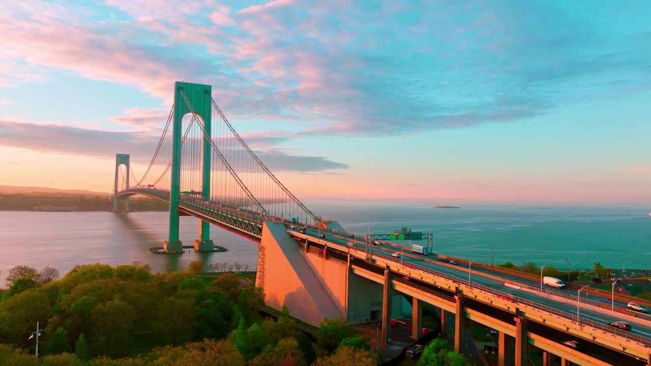 Vista aérea a la hora dorada del Puente Bronx-Whitestone en la ciudad de Nueva York, con tráfico fluyendo por el puente colgante sobre el East River bajo un suave cielo vespertino pastel.