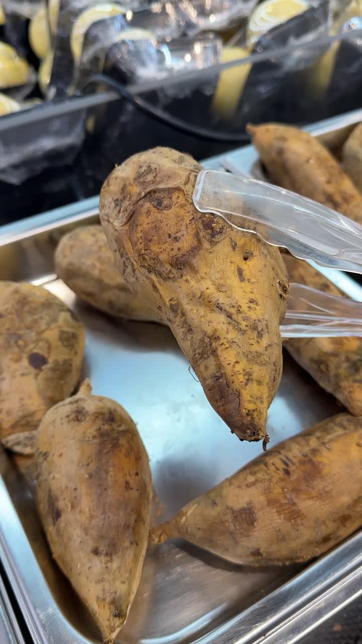 Mano che prende una patata dolce con le pinze in un vassoio espositivo