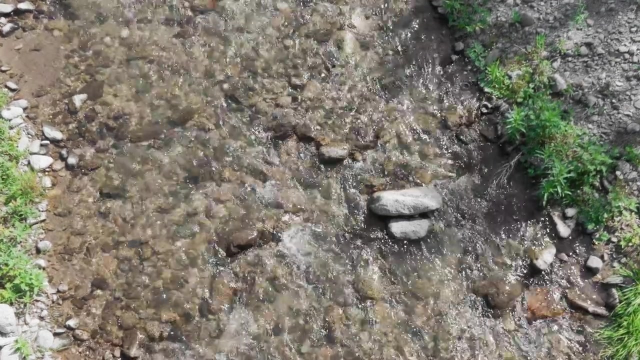 Acqua di fiume che scorre su rocce bianche, ripresa statica con treppiede. Veduta dall'alto ad angolo elevato di un limpido ruscello di montagna che scorre su pietre e ciottoli del letto del fiume